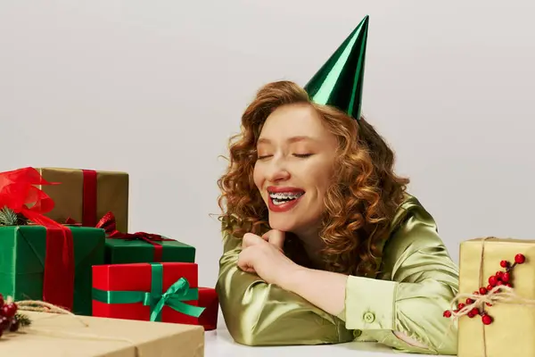 A cheerful young woman enjoys posing surrounded by vibrant holiday gifts and decorations. — Stock Photo