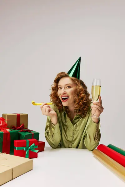 A young woman wearing a party hat surrounded by presents and festive decor. — Stock Photo