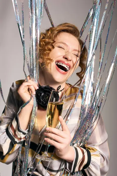 A young woman happily posing cheerfully with champagne in hand, amid festive decorations. — Stock Photo