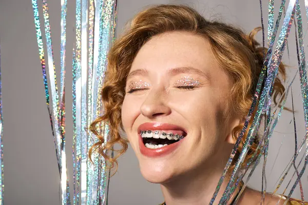 A young woman smiles brightly while posing actively, surrounded by shiny decorations. — Stock Photo
