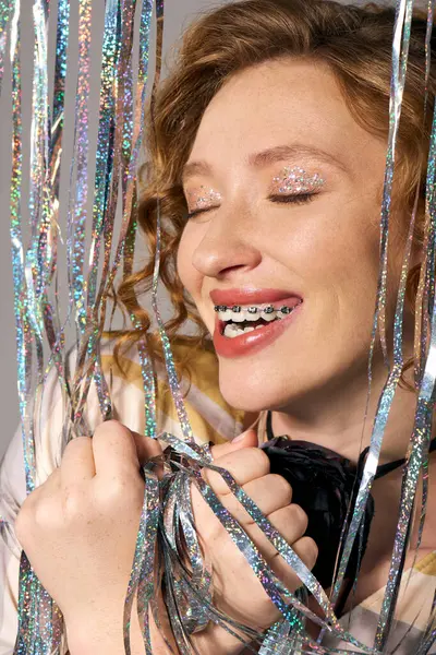 A young woman expresses delight while posing cheerfully with shiny, colorful decorations in her hands. — Stock Photo