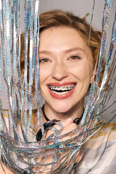A cheerful young woman smiles broadly while playfully surrounded by sparkling ribbons. — Stock Photo