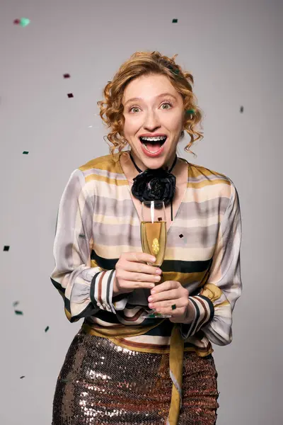Una giovane donna felice tiene un bicchiere di champagne, circondata da coriandoli colorati in una celebrazione. — Foto stock