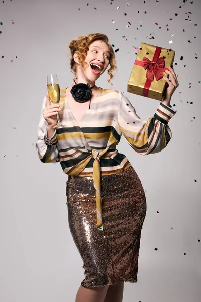 Una giovane donna felice tiene un regalo e un drink, godendo di una festa con coriandoli.. — Foto stock