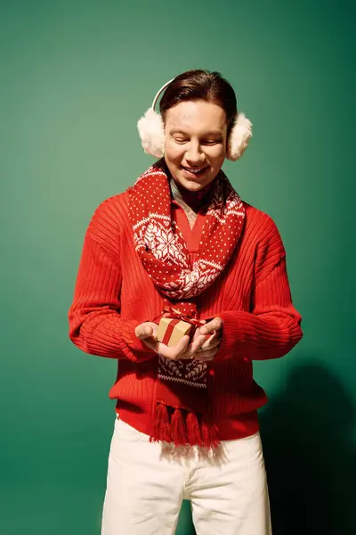 A young man in a vibrant red sweater eagerly opens a small present, smiling cheerfully. — Stock Photo