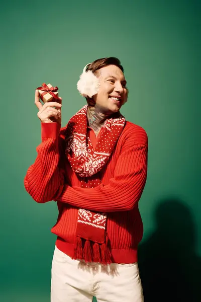 A tattooed young man smiles with a wrapped gift, ready for winter festivities. — Stock Photo