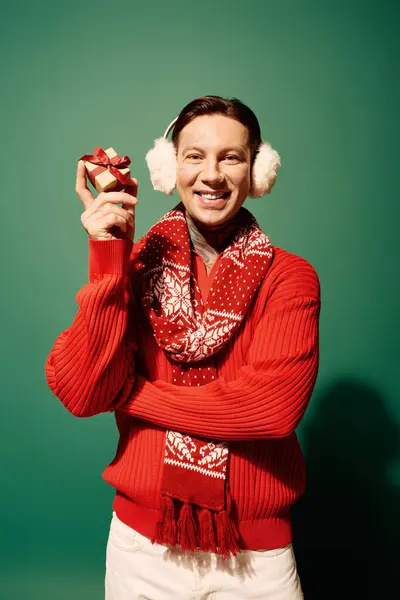 A joyful young man, wearing earmuffs and a vibrant scarf, presents a wrapped gift. — Stock Photo