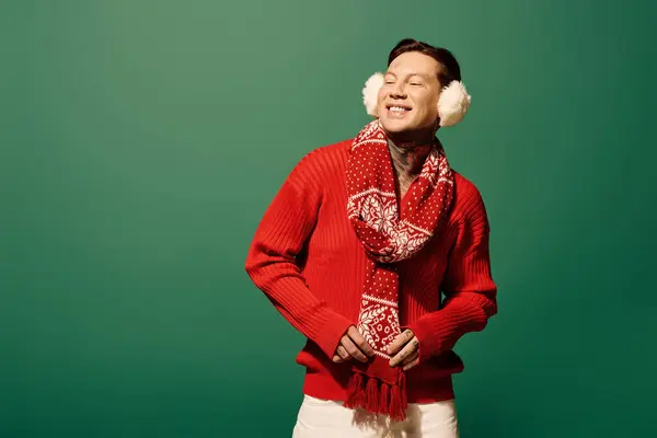 Le jeune homme pose ludique dans un pull rouge vibrant avec une écharpe chaude et des cache-oreilles moelleux. — Photo de stock