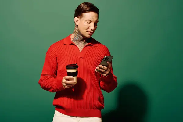 Un joven sostiene una taza de café y mira su teléfono inteligente en un fondo colorido. - foto de stock