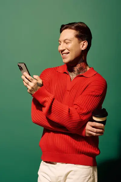 A smiling young man with tattoos checks his phone while holding a coffee cup, exuding happiness. — Stock Photo