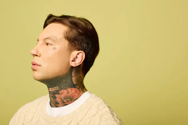 A young man with distinctive tattoos showcases his profile against a soothing green wall. — Stock Photo