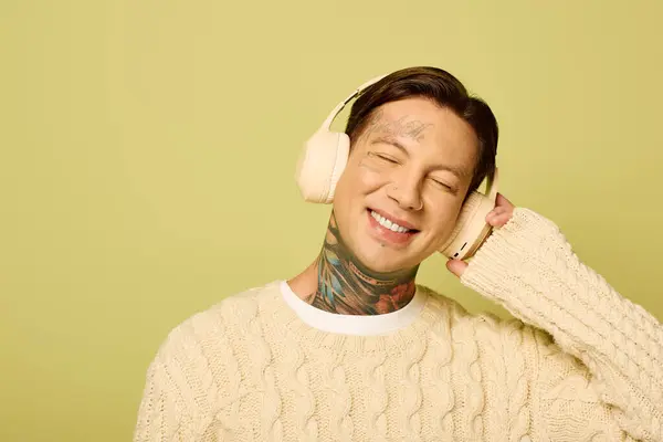 Un jeune homme joyeux avec des tatouages écoute de la musique, affichant une expression joyeuse et un style confortable. — Photo de stock
