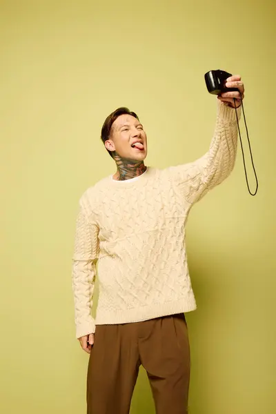 Un joven con tatuajes posa juguetonamente mientras toma una selfie con una cámara. - foto de stock