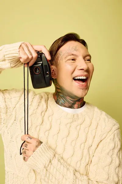 El joven vibra de alegría mientras posa juguetonamente con una cámara clásica, mostrando sus tatuajes. - foto de stock