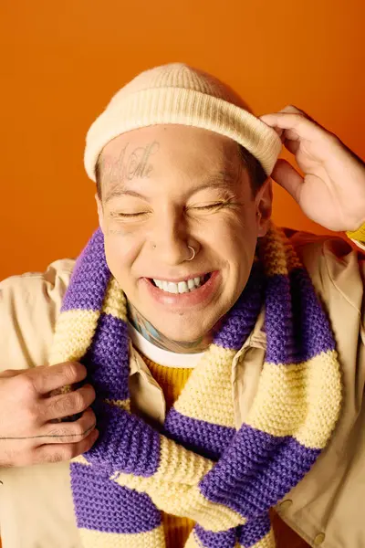 A cheerful young man with tattoos wears a knit hat and striped scarf while grinning widely. — Stock Photo