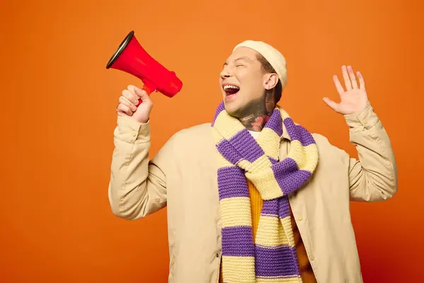 The young man with colorful tattoos expresses joy while holding a megaphone and wearing a scarf. — Stock Photo