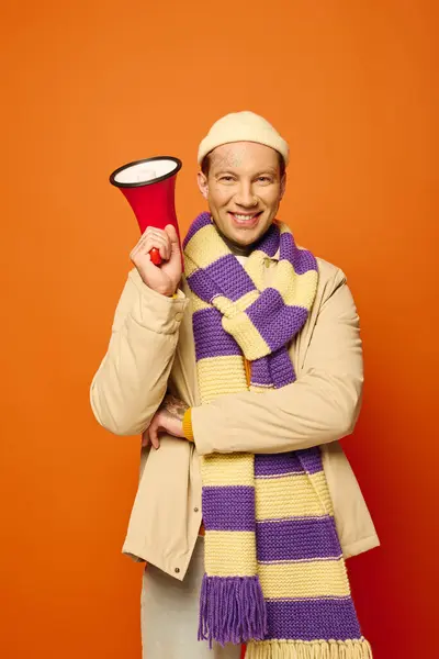 A joyful young man wearing a scarf and beanie holds a megaphone, ready to engage the crowd. — Stock Photo