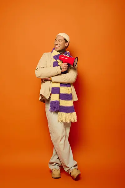 A casually dressed young man playfully leans with a megaphone, radiating creativity. — Stock Photo