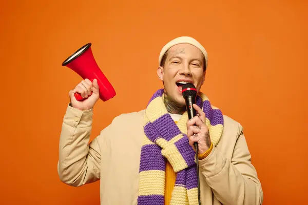 A young man with tattoos is energetically speaking into a microphone while holding a megaphone. — Stock Photo