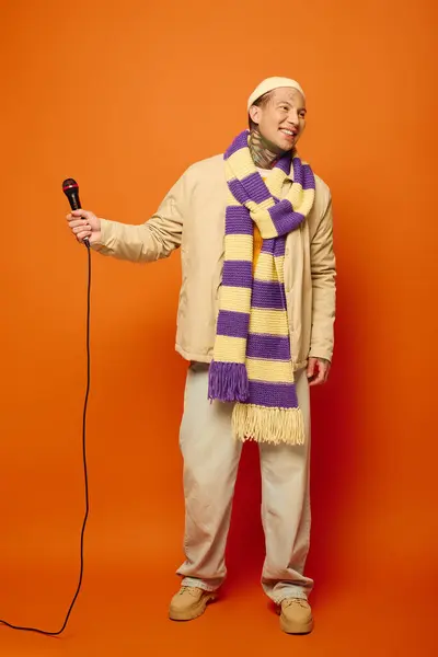 A young man wearing a scarf and seasonal attire and holding microphone. — Stock Photo