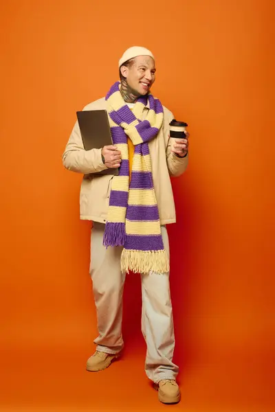 A young man smiles as he holds a cup of coffee and a notebook, dressed for the season. — Stock Photo