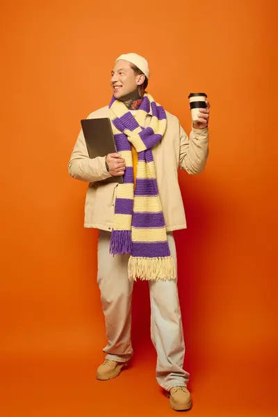 A cheerful young man holds a cup and notebook, showcasing his tattoos in a cozy outfit. — Stock Photo