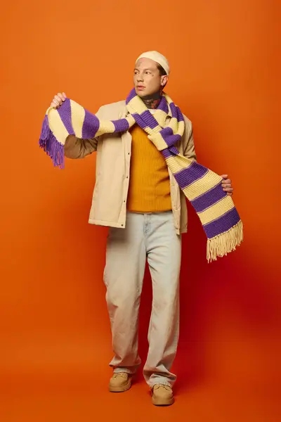 A young man with tattoos confidently poses while holding a colorful scarf in a striking setting. — Stock Photo