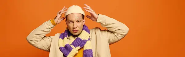 A young man adjusts his scarf with tattoos visible on his arms, framed by an orange backdrop. — Stock Photo
