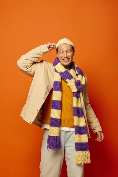 A young man playfully adjusts his hat while showcasing his tattoos and a striped scarf. — Stock Photo