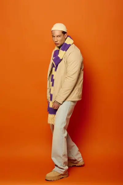 A young man flaunts his tattoos against a bright orange background in stylish attire. — Stock Photo