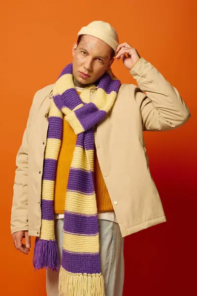 A stylish young man shows off a vibrant scarf, tattoos, and adjusts his hat. — Stock Photo