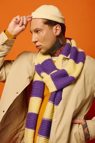 A stylish young man wearing a beanie and patterned scarf poses confidently in a vibrant setting. — Stock Photo