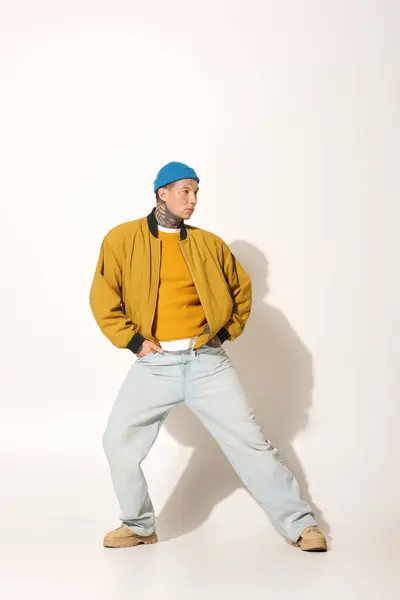 A young man with striking tattoos stands confidently in a yellow sweater and jacket. — Stock Photo
