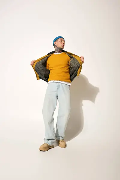 A young man with tattoos confidently displays his casual outfit, revealing his vibrant sweater — Stock Photo