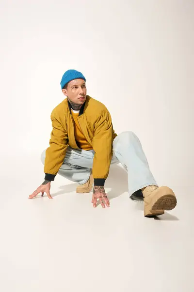 A tattooed young man poses creatively on a light background while wearing casual attire. — Stock Photo