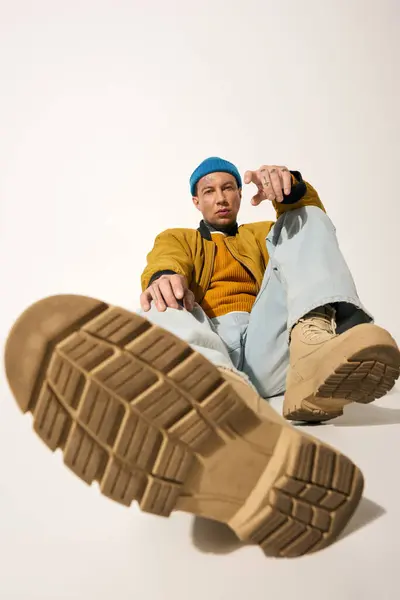 A young man highlights his trendy footwear while sitting confidently on a simple backdrop. — Stock Photo