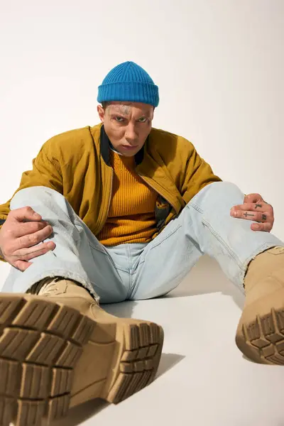 A young man with tattoos poses confidently while seated on a smooth surface, showcasing his fashion. — Stock Photo