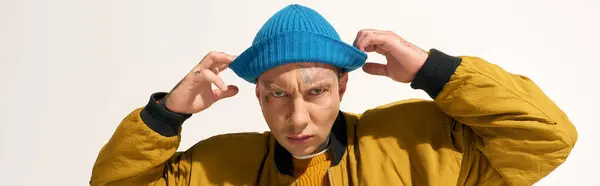 The young man showcases his tattoos while playfully adjusting a bright blue hat indoors. — Stock Photo