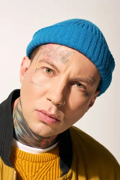 A young man with striking tattoos gazes directly at the camera while wearing a blue beanie. — Stock Photo