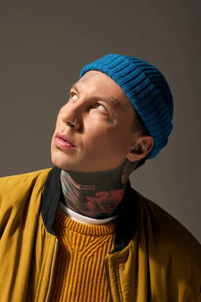 Il giovane con un berretto blu mostra i suoi tatuaggi vivaci e il suo vestito accogliente. — Foto stock