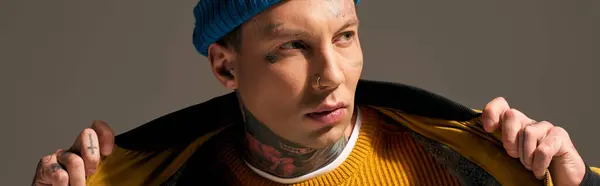 Un jeune homme à la mode avec des tatouages distinctifs et un chapeau lumineux ajuste sa veste. — Photo de stock