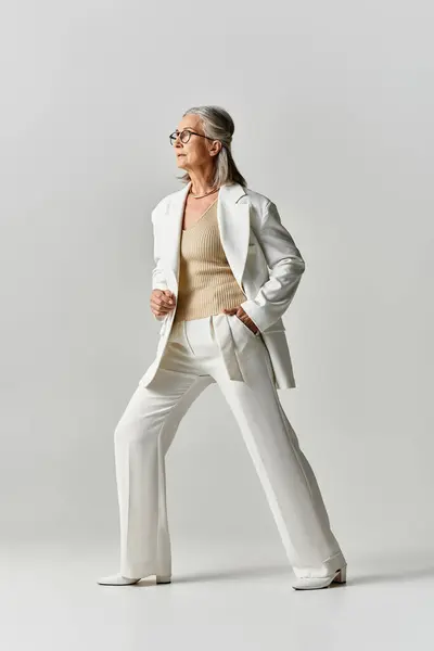 Une femme gracieuse aux cheveux gris met en valeur l'élégance dans un costume blanc sur mesure, respirant la confiance et le style. — Photo de stock