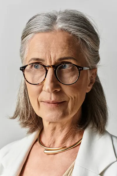 A mature woman with beautiful grey hair showcases her elegance in a stylish white suit and glasses. — Stock Photo