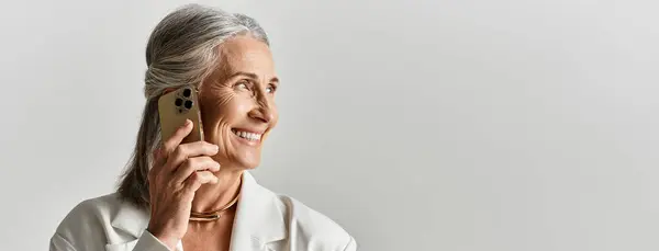 Una donna matura elegante trasuda fiducia mentre parla con grazia sul suo telefono, vestita di bianco. — Foto stock