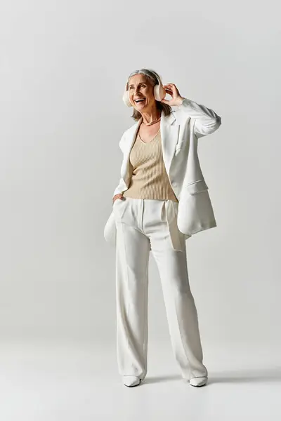 In mezzo a un tranquillo sfondo grigio, una graziosa donna matura mostra la sua eleganza in un abito bianco. — Foto stock