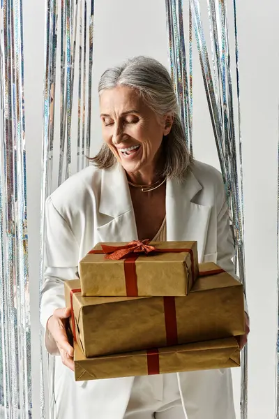 A cheerful mature woman embraces the joy of the holidays, holding beautifully wrapped gifts in a festive setting. — Stock Photo