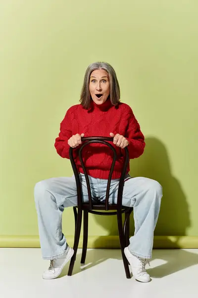 A joyful mature woman with grey hair showcases winter fashion in a bright red sweater, exuding confidence. — Stock Photo