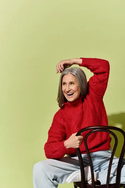 Eine fröhliche reife Frau mit grauen Haaren präsentiert Wintermode und strahlt in ihrem roten Pullover Wärme und Stil aus.. — Stockfoto