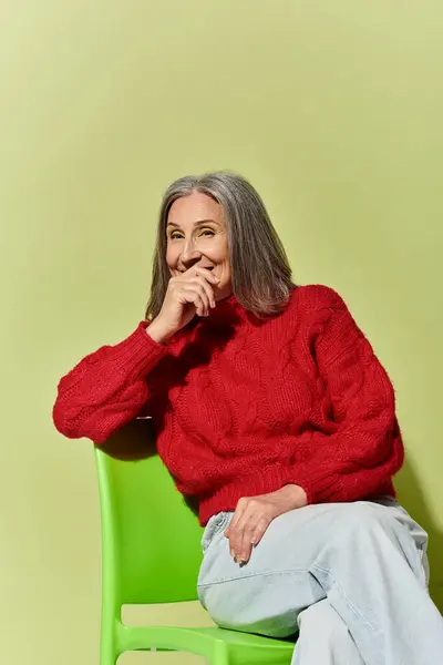 A stylish mature woman with grey hair smiles warmly, showcasing winter fashion in a cozy red sweater. — Stock Photo