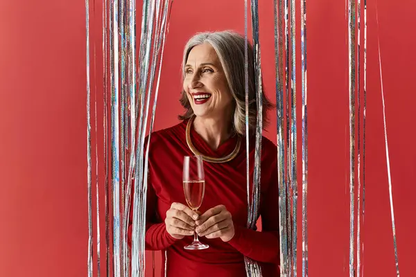 A beautiful mature woman with grey hair smiles joyfully while holding a glass, celebrating the festive season. — Stock Photo